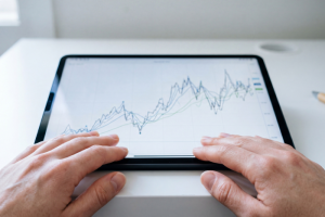 Primer plano de unas manos utilizando una tablet colocada en horizontal sobre una mesa blanca, donde se muestra un gráfico de líneas con las fluctuaciones y la evolución del precio de la luz de la tarifa regulada PVPC de Energía XXI.