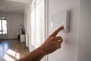 Mano activando el panel de control blanco de un sistema de alarma de seguridad en la pared de una vivienda.