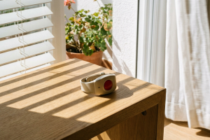 Pulsera de teleasistencia o botón de emergencia rojo sobre una mesa de madera iluminada por la luz de la ventana.