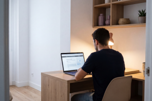 Hombre sentado frente a un ordenador portátil en su escritorio gestionando trámites online desde casa.
