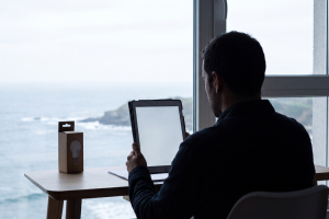 Hombre frente a una ventana con vistas al mar consultando una tablet junto a una caja de bombilla LED.