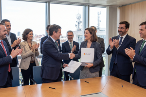Dos representantes estrechan la mano sosteniendo una carpeta de la CNMC rodeados de un equipo de personas aplaudiendo en una sala de reuniones.