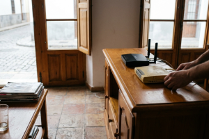 Manos manipulando los cables de red de un router Wi-Fi sobre un mueble de madera junto a un ventanal.