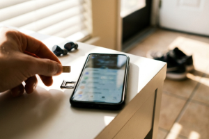 Mano sosteniendo una tarjeta nano SIM junto a un smartphone con la bandeja de extracción abierta sobre un mueble blanco.