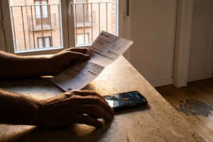 Manos sujetando una factura en papel sobre una mesa junto a un smartphone que muestra una gráfica de consumo.