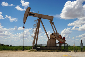 Balancín de extracción de petróleo funcionando en un campo petrolífero bajo un cielo azul con nubes.
