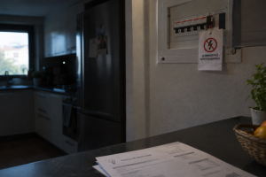 Cuadro eléctrico de vivienda a oscuras con cartel de suministro interrumpido y factura de electricidad en la mesa.