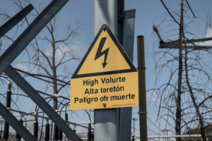 Señal amarilla de advertencia de alto voltaje en una torre metálica de una subestación eléctrica.